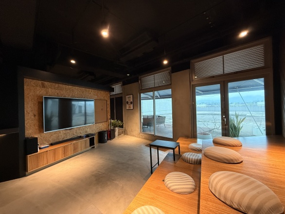 The lounge, with a long wooden table, floor cushions and a TV
